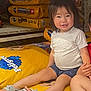 Koa is registered to the contest to win money with this photo: child, toddler, smiling, sitting, pedigree, dog_food, store, aisle, yellow_bags, sandals, clothing, shorts, white_shirt, hair, face, person, retail, shopping, footwear, indoor