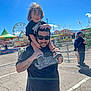 Koa joined the competition — help win amazing prizes! child, man, carnival, outdoor, sunny, blue_sky, ferris_wheel, tent, ride, clothing, sunglasses, smiling, person, fun, festival, family, daytime, tattoo, holding, shoulders