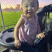 Kaili joined the competition — help win amazing prizes! toddler, child, stroller, pink_dress, smiling, park, sunset, chain_link_fence, green_field, outdoor, person, baby, happy, evening, nature, grass, seat, hand, portrait, cute