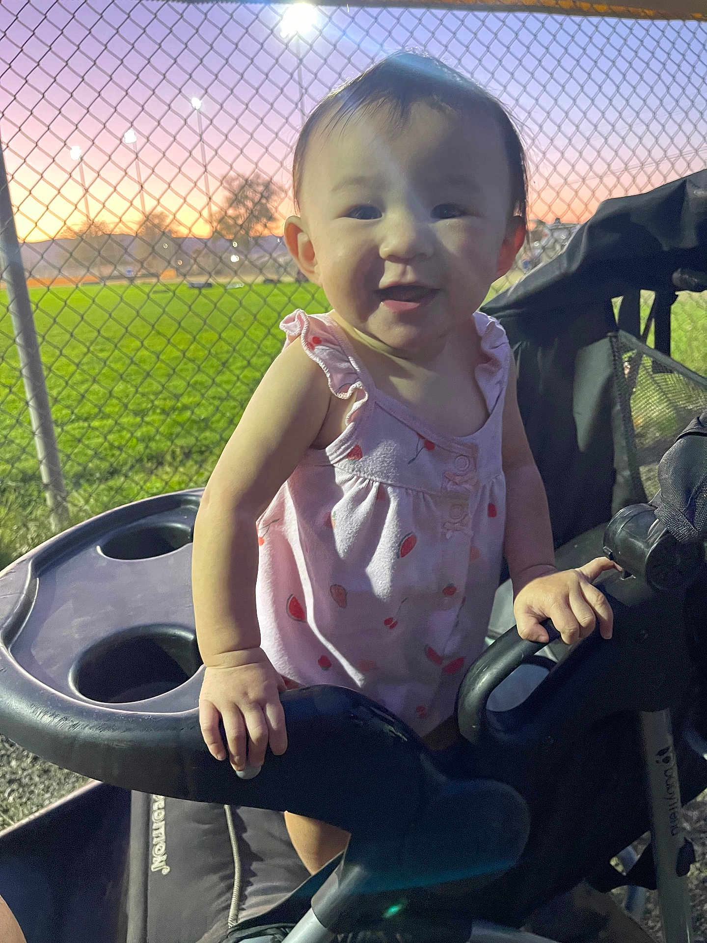 Kaili joined the competition — help win amazing prizes! toddler, child, stroller, pink_dress, smiling, park, sunset, chain_link_fence, green_field, outdoor, person, baby, happy, evening, nature, grass, seat, hand, portrait, cute