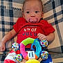 Penelope is registered to the contest to win money with this photo: baby, infant, pacifier, plush_toy, red_clothing, blue_clothing, american_flag_pattern, blanket, lying_down, cute, child, celebration, holiday_outfit, colorful, patterned, indoor, person, portrait, small_hand, cozy
