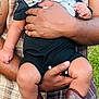 adult, baby, bib, black_outfit, boots, casual_clothing, child, curly_hair, cute, grass, hands, happy, holding, joyful, laughing, outdoor, person, plaid_shirt, portrait, smiling