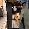 cat, tabby_cat, chair, wooden_table, coat, indoor, tile_floor, curious, pet_toy, furniture, domestic_animal, household, cozy, black_chair, playful, animal, looking, floor, living_room, domestic_life