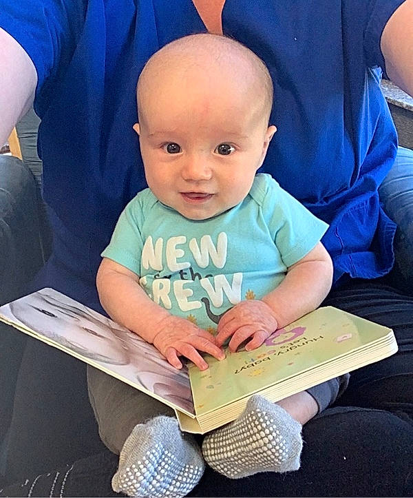 Sterling is registered to the contest to win money with this photo: baby, baby_products, baby_toddler_clothing, book, child, comfort, electric_blue, electronic_device, eye, fun, happy, lap, netbook, people, person, product, reading, sitting, smile, t_shirt