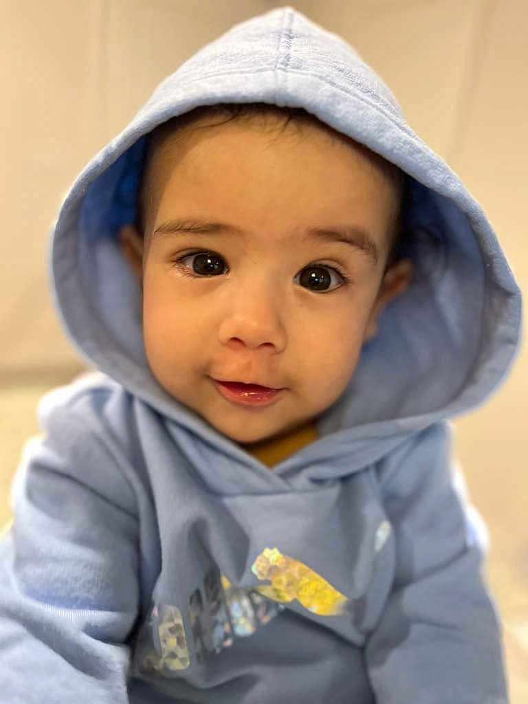 Dereck Isamel joined the competition — help win amazing prizes! baby, child, hoodie, blue_clothing, face, eyes, portrait, cute, infant, young_child, sitting, indoors, soft_lighting, casual_clothing, smiling, person, closeup, headwear, warm_clothing, adorable