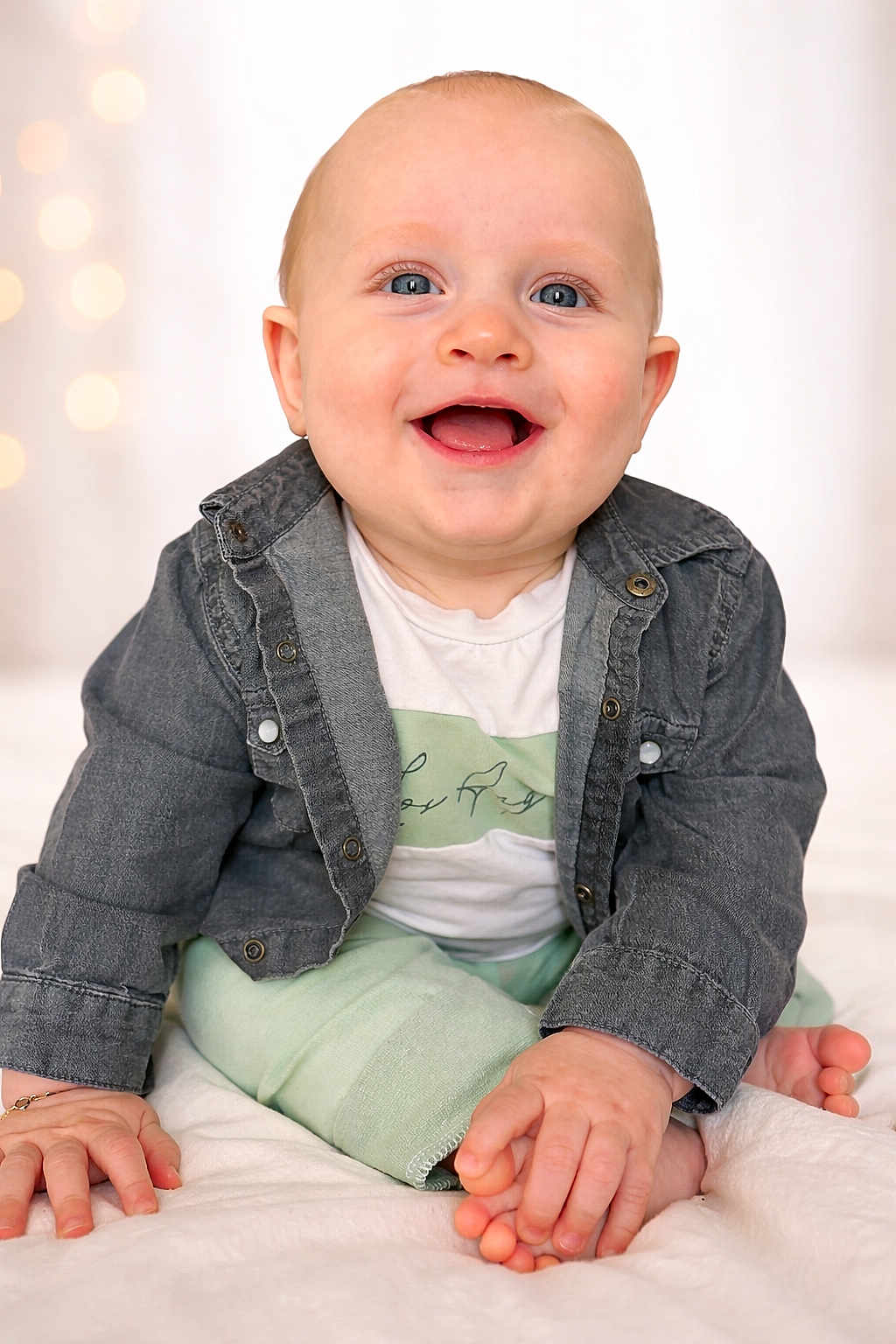 Elio participe au concours pour gagner de l'argent avec cette photo : baby, infant, smiling, sitting, denim_jacket, onesie, bare_feet, toes, hands, blue_eyes, happy, portrait, studio_background, bokeh, blanket, crawling_pose, cheerful, close_up, skin, cute