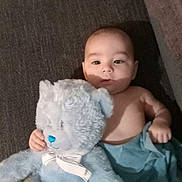 Tommy joined the competition — help win amazing prizes! baby, teddy_bear, plush_toy, blanket, sofa, couch, infant, child, indoor, cute, soft_toy, blue, person, face, hand, lying_down, cozy, smiling, young, comfort