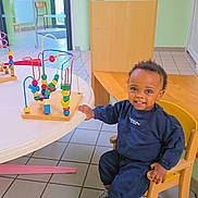 David Afanbo a rejoint le concours — aidez-le/la à gagner de superbes lots ! child, toddler, smiling, indoor, playroom, toy, bead_maze, table, chair, wooden_furniture, floor_tiles, casual_clothing, sneakers, young_child, colorful_toys, happy, person, play, daylight, interior