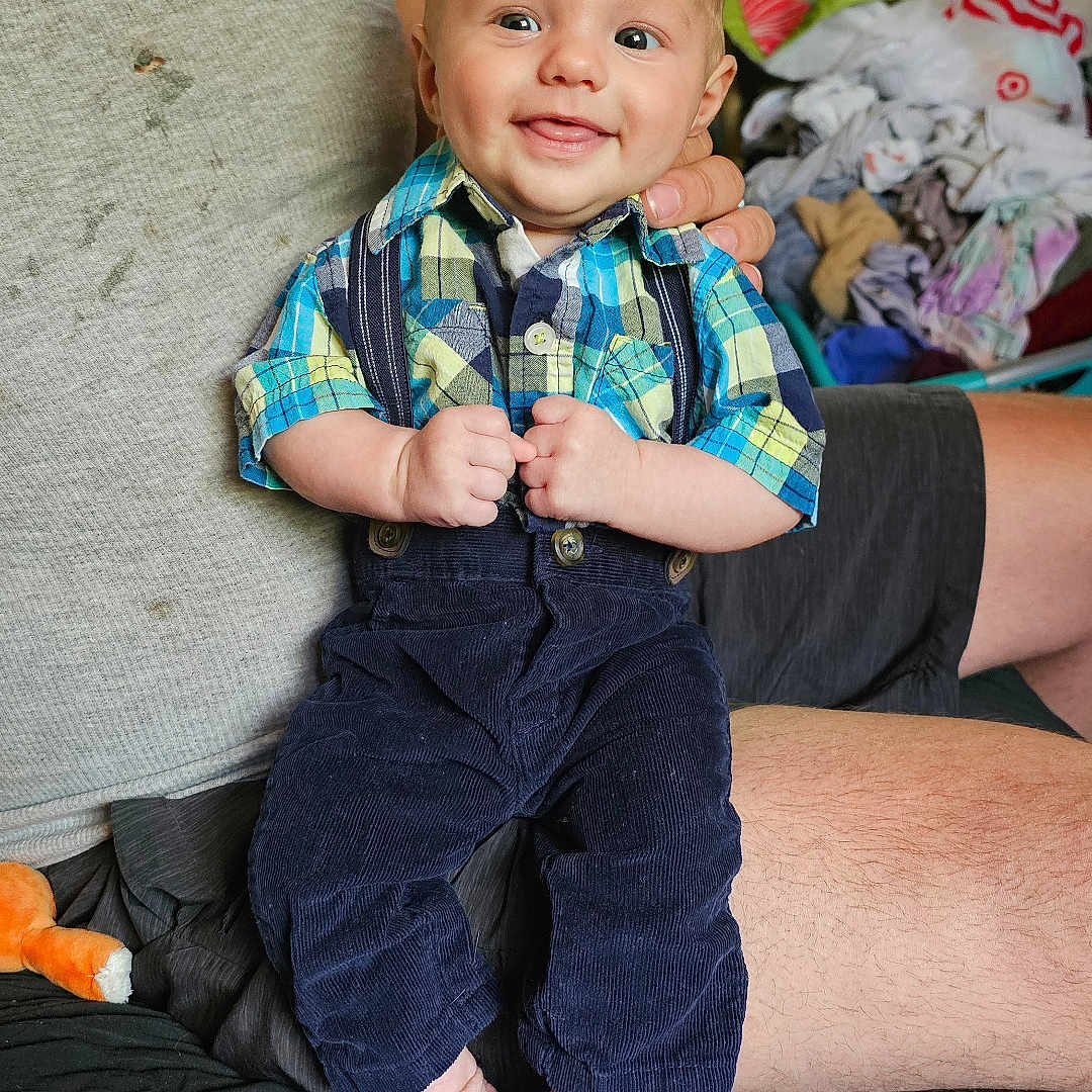 Niko is registered to the contest to win money with this photo: baby, bodypart, clothing, coat, couch, face, finger, furniture, hand, happy, head, jacket, jeans, pants, person, photography, portrait, shorts, sitting, smile