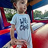 toddler, child, onesie, wild_child, bounce_house, indoor, hand_holding, tattoo, curly_hair, play, red, blue, yellow, outdoor_background, trees, car, netting, footwear_bare, person, portrait