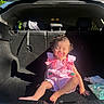 toddler, child, car_trunk, pink_dress, pacifier, sunlight, baby_wipes, diapers, sitting, smiling, cute, hair_tie, car_interior, shadow, playful, casual, daylight, infant, happy, young_child