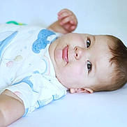 Moses is registered to the contest to win money with this photo: arm, baby, child, closeup, cute, eyes, face, hand, indoor, infant, lying_down, onesie, peaceful, portrait, short_hair, skin, smile, soft_light, white_background, young