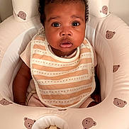 Alayna joined the competition — help win amazing prizes! baby, infant, child, portrait, sitting, wide_eyes, curly_hair, facial_expression, bib, striped_clothing, pink_clothing, baby_seat, nursery, cushion, bear_pattern, indoor, warm_lighting, closeup, adorable, photography