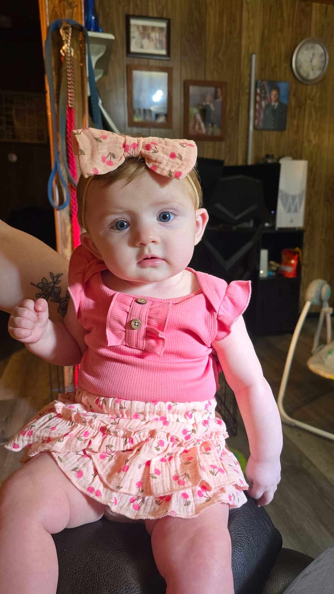 Scarlet is registered to the contest to win money with this photo: baby, child, girl, pink_clothing, headband, bow, sitting, indoor, tattoo, wood_paneling, furniture, skirt, blue_eyes, person, portrait, cute, holding_hand, decor, clock, photography