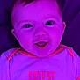 baby, child, face, smile, clothing, purple_light, infant, happy, cute, person, text_on_clothing, short_sleeves, young_child, portrait, indoors, bright_eyes, shirt, neon_light, closeup, joy