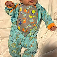 Emani joined the competition — help win amazing prizes! baby, blanket, blue_clothing, child, cute, dinosaur_print, expression, fabric, footed_pajamas, hand, indoor, infant, lying_down, onesie, orange_trim, person, portrait, sleepwear, white_background, young_child