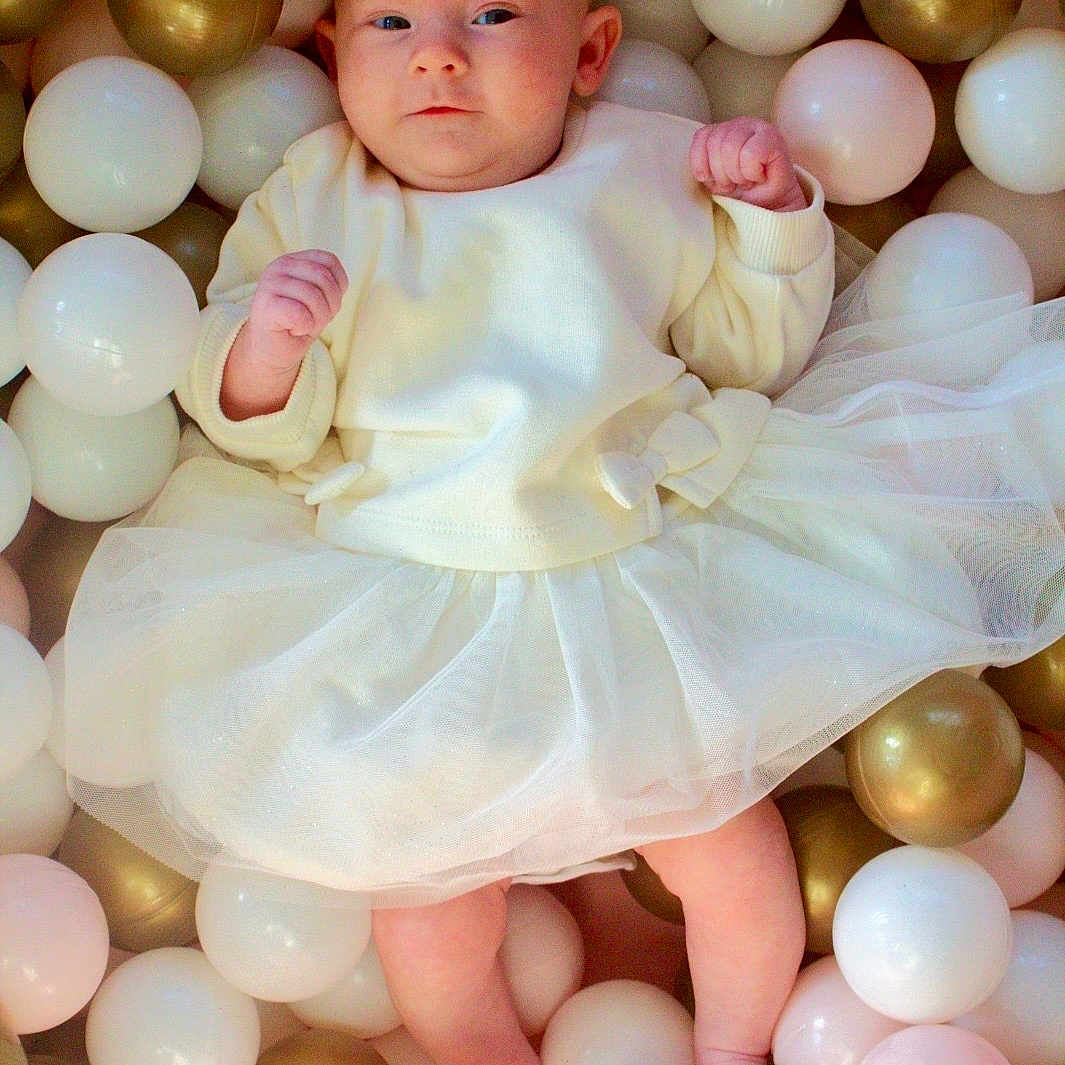 Pennie-Mae joined the competition — help win amazing prizes! baby, ball_pit, child, clothing, cute, eyes, feet, fists, gold_balls, head, indoor, infant, newborn, pastel_colors, plastic_balls, playful, portrait, skin, soft_lighting, white_dress
