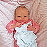 baby, newborn, infant, pink_blanket, pink_clothing, onesie, soft_texture, cute, cozy, sleepy_animal, embroidered_text, portrait, indoor, closeup, child, face, hand, lying_down, person, warm