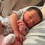 Oakland is registered to the contest to win money with this photo: baby, infant, newborn, sleeping, couch, floral_clothing, hand, foot, sock, resting, cozy, indoor, person, skin, face, parent, comfort, soft_lighting, home, relaxation