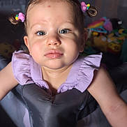 Kira joined the competition — help win amazing prizes! toddler, child, girl, playpen, toys, indoor, face, blue_eyes, hair_ties, curly_hair, purple_dress, expression, puzzled, baby, person, young_child, play_area, daylight, home, cute