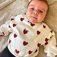 Ophélya a rejoint le concours — aidez-le/la à gagner de superbes lots ! amour, baby, black_pants, casual_clothing, child, comfortable, cute, face, happy, indoors, infant, lying_down, portrait, red_hearts, smiling, soft_texture, towel, warm_colors, white_sweater, young_child