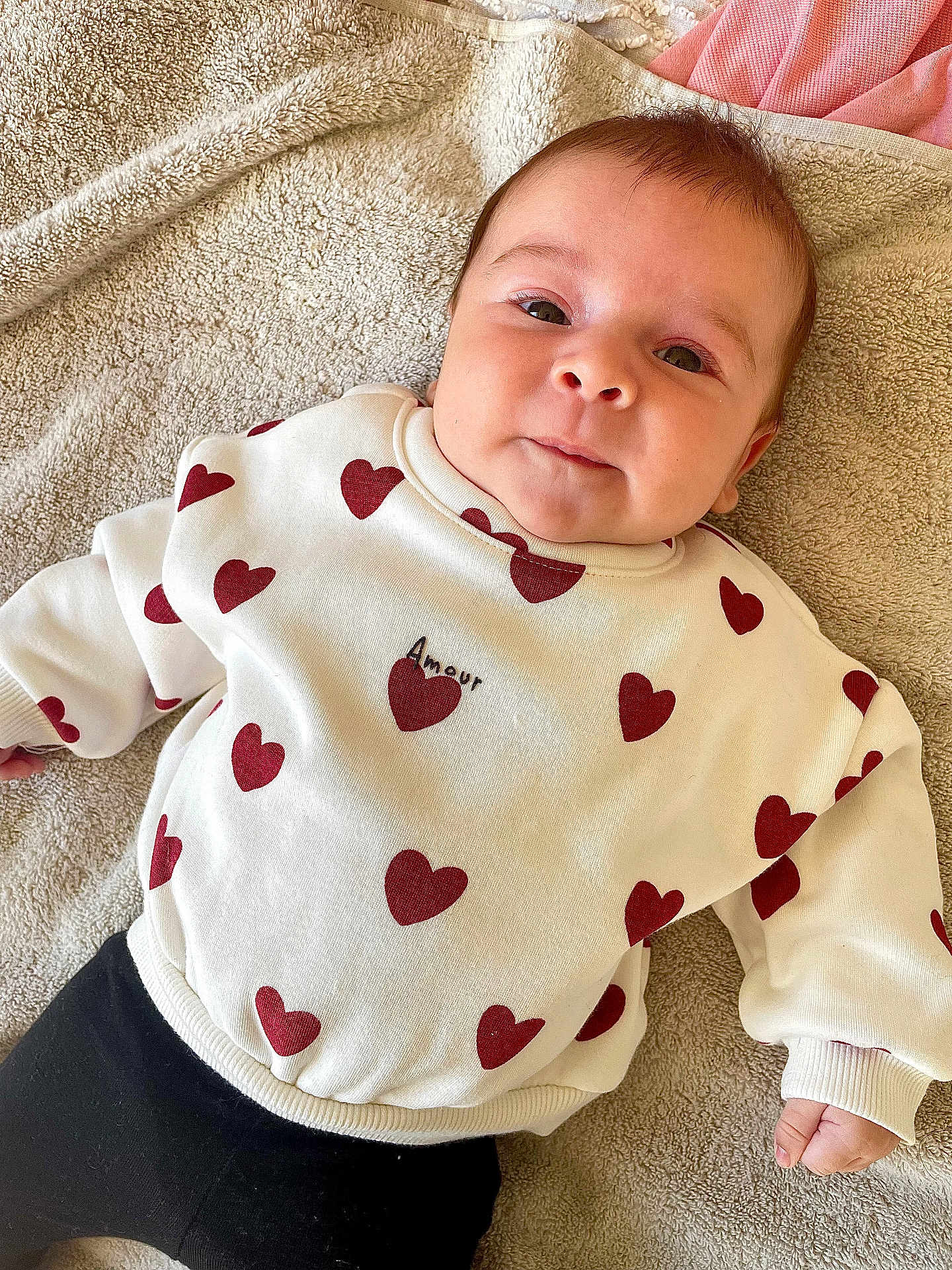 Ophélya a rejoint le concours — aidez-le/la à gagner de superbes lots ! amour, baby, black_pants, casual_clothing, child, comfortable, cute, face, happy, indoors, infant, lying_down, portrait, red_hearts, smiling, soft_texture, towel, warm_colors, white_sweater, young_child