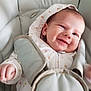 baby, infant, smile, hoodie, car_seat, straps, cushion, clothing, face, hand, happy, child, portrait, indoor, cute, young, person, seatbelt, comfort, closeup