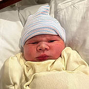 Orion is registered to the contest to win money with this photo: newborn, baby, infant, child, portrait, face, eyes_open, serious_expression, knit_cap, striped_hat, cream_outfit, blanket, swaddled, bedding, hospital, indoor, close_up, sitting, soft_lighting, photography