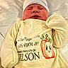 newborn, baby, infant, sleeping, portrait, hospital, hospital_bed, onesie, baby_clothing, knit_cap, striped_hat, blanket, swaddled, face, closed_eyes, peaceful, cartoon, pumpkin, text_on_clothing, indoor