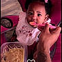 baby, child, feeding, high_chair, spoon, baby_food, pink, hair_bows, bib, hands, tattoo, container, heart_doodle, indoor, person, cute, expression, face, closeup, seat