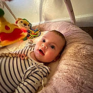 Andie joined the competition — help win amazing prizes! baby, infant, striped_clothing, plush_bed, toy, colorful_toy, face, person, indoor, wall, curious, lying_down, soft_texture, child, playtime, pacifier_clip, head, eyes, mouth_open, comfort