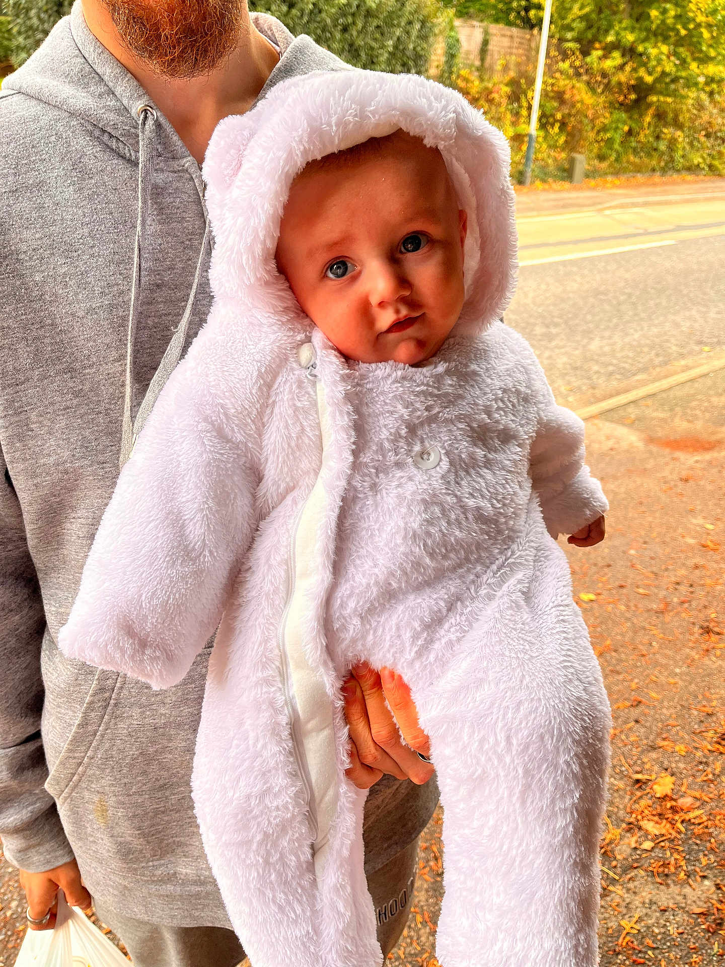 Merlin is registered to the contest to win money with this photo: baby, child, person, hooded_clothing, adult, outdoor, fall, leaves, road, trees, greenery, coat, zipper, hand, beard, casual_clothing, cute, warm_clothing, expression, holding