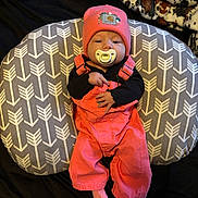 Melissa is registered to the contest to win money with this photo: baby, infant, pacifier, pink_overalls, beanie, cushion, blanket, patterned, indoor, resting, cute, clothing, portrait, child, soft, cozy, sleepy, small_hands, fabric, laying_down