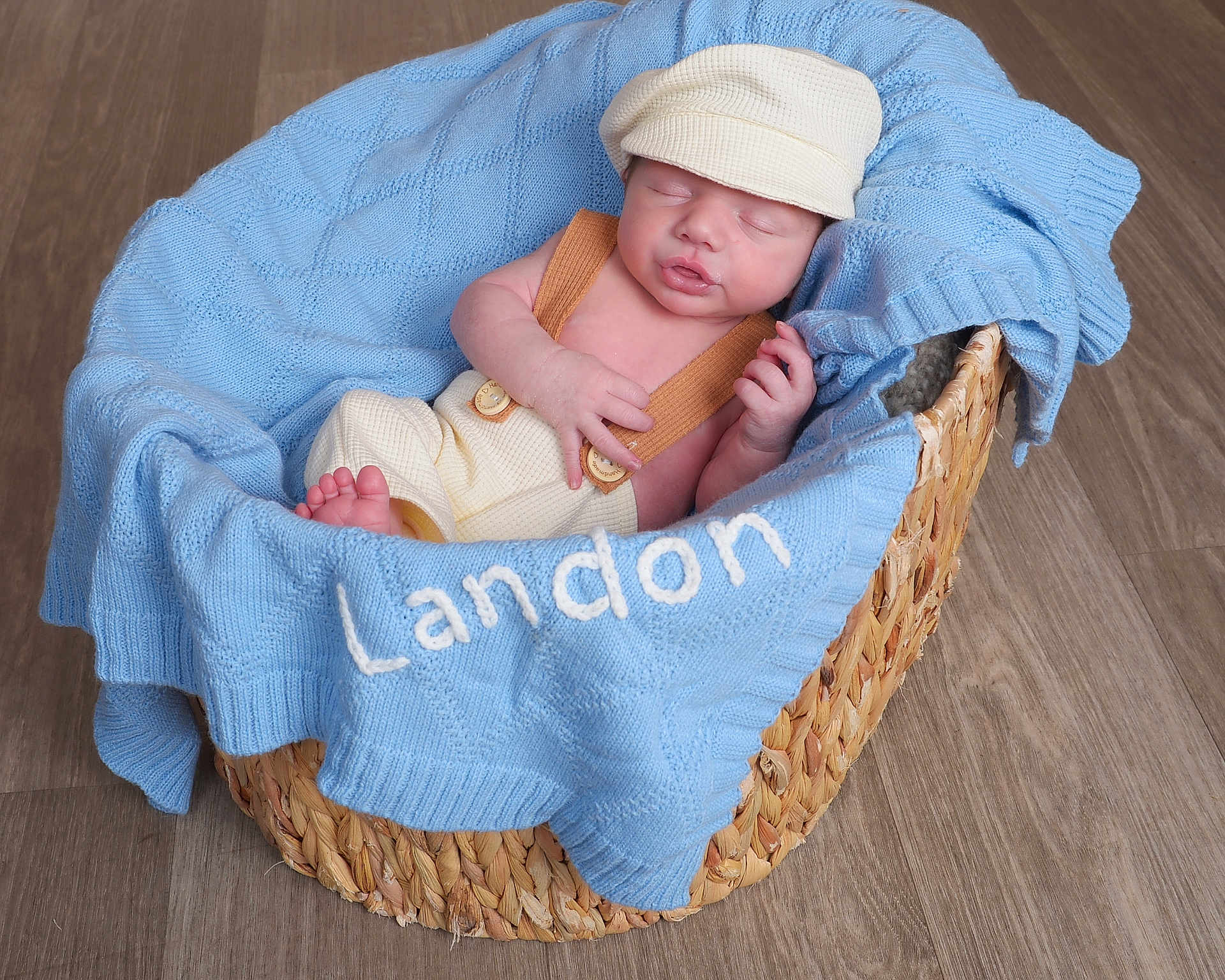 Landon is registered to the contest to win money with this photo: newborn, baby, basket, blanket, blue, cap, clothing, floor, infant, knit, laying, peaceful, portrait, resting, suspenders, toddler, wood, young, cute, cozy