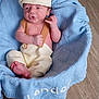 Landon is registered to the contest to win money with this photo: baby, infant, newborn, basket, blue_blanket, knitted_blanket, wooden_floor, baby_clothes, cap, pout, cute, cozy, portrait, indoors, soft_texture, child, person, small_feet, expression, resting