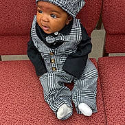 Elijah is registered to the contest to win money with this photo: baby, child, infant, hat, bow_tie, checkered_clothing, black_and_white, sitting, red_chair, patterned_fabric, cute, portrait, indoors, clothing, footwear, sock, young_child, face, curious, seated