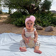 Layla is registered to the contest to win money with this photo: baby, infant, child, outdoor, blanket, flower_headband, sign, nature, greenery, rocks, tree, desert, sunlight, sitting, cute, portrait, clothing, pink, white, person