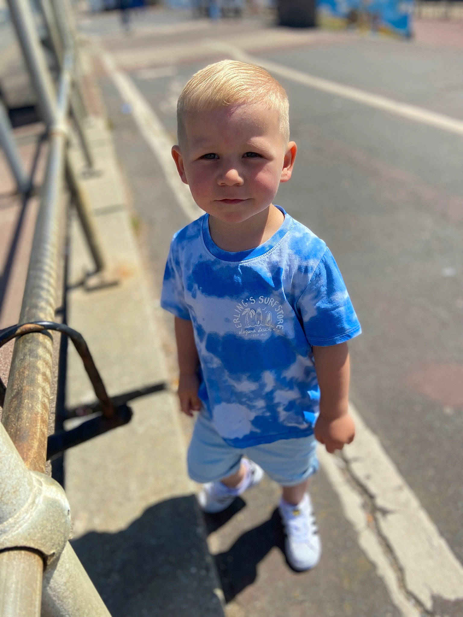 Maison is registered to the contest to win money with this photo: baby_toddler_clothing, chin, cool, facial_expression, fun, hairstyle, happy, joint, leisure, mammal, person, public_space, recreation, shorts, skin, sleeve, smile, sneakers, standing, toddler