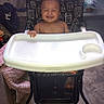 baby, child, high_chair, smiling, grinning, toothy_smile, seated, indoor, portrait, infant, happy, face, bare_shoulders, tray, furniture, patterned_chair, home, carpet, curtain, candid_photo