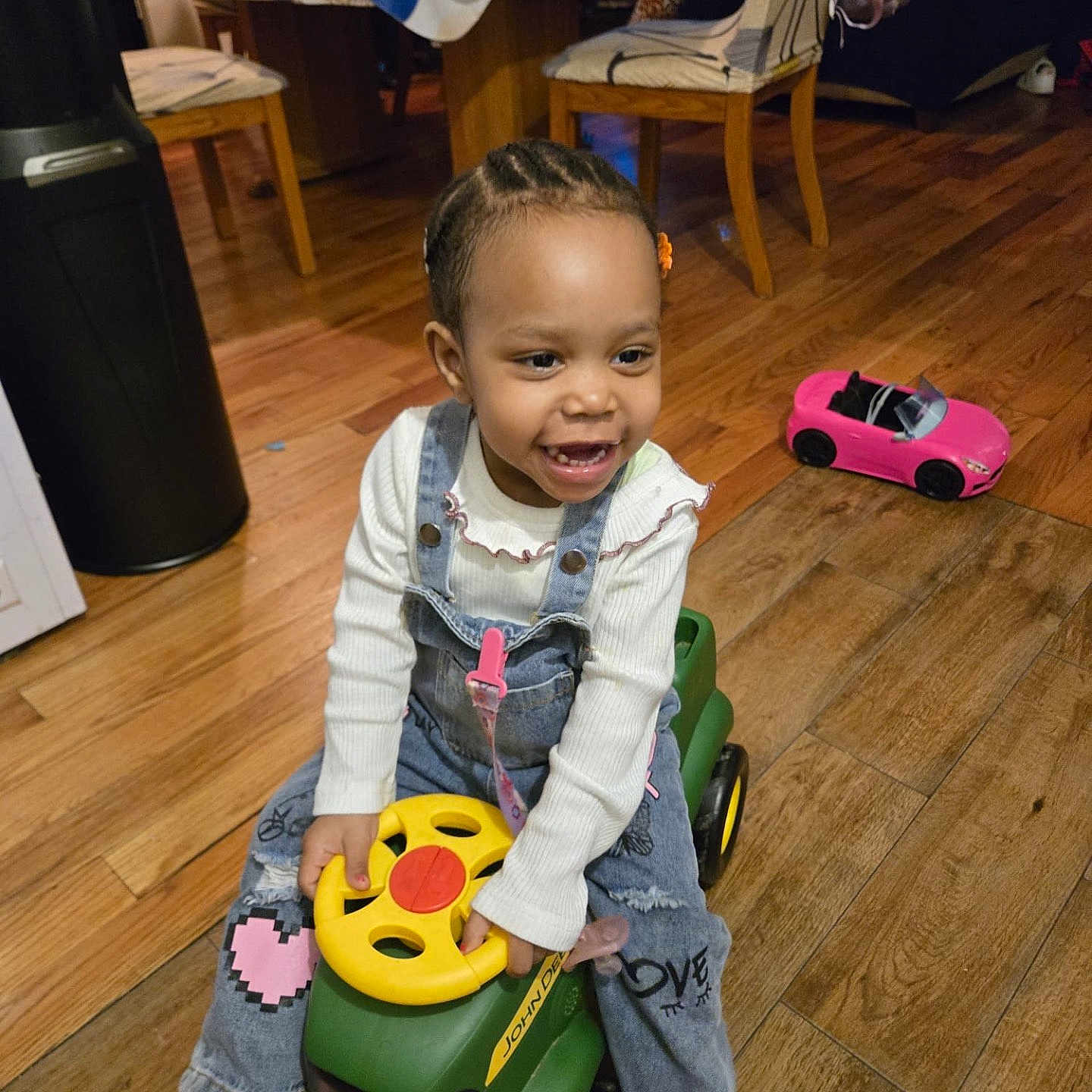 Kaylee joined the competition — help win amazing prizes! braided_hair, casual_clothing, chair, child, denim_overalls, dining_table, flower_hair_clip, happy, home, indoor, john_deere, pink_toy_car, playtime, ride_on_toy, smiling, striped_socks, tablecloth, toddler, toy, wooden_floor