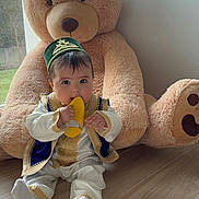 Noah a rejoint le concours — aidez-le/la à gagner de superbes lots ! baby, chewing, child, cute, daylight, floor, hat, home, indoor, large_toy, person, plush, sitting, stuffed_animal, teddy_bear, toy, traditional_clothing, window, wooden_floor, yellow_shoe