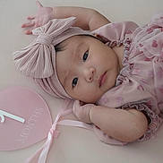 Azyla is registered to the contest to win money with this photo: baby, infant, pink, headband, bow, heart_shaped_sign, 1_month, milestone, cute, portrait, lying_down, soft_texture, child, young, adorable, close_up, peaceful, clothing, fabric, ribbon