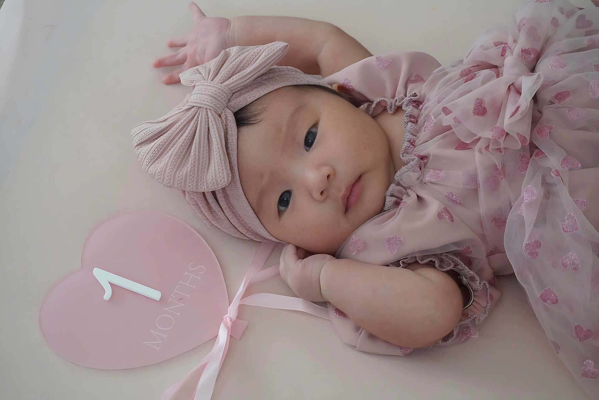 Azyla is registered to the contest to win money with this photo: baby, infant, pink, headband, bow, heart_shaped_sign, 1_month, milestone, cute, portrait, lying_down, soft_texture, child, young, adorable, close_up, peaceful, clothing, fabric, ribbon