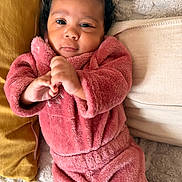 Ashanti a rejoint le concours — aidez-le/la à gagner de superbes lots ! baby, blanket, child, couch, cozy, curly_hair, cute, face, fluffy_clothing, hands, indoor, infant, person, pillow, pink_outfit, portrait, relaxed, smiling, soft_texture, young