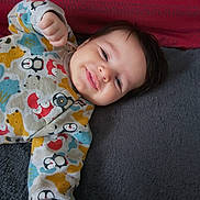 Paul participe au concours pour gagner de l'argent avec cette photo : baby, infant, smile, face, onesie, patterned_clothing, penguin, bear, fox, hand, hair, lying_down, blanket, pillow, cozy, cute, portrait, indoor, closeup, toddler