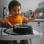 toddler, child, high_chair, cake, smiling, happy, orange_shirt, food, celebration, birthday, indoors, table, face, arms_raised, feet, photography, monochrome_background, baby, sitting, fun