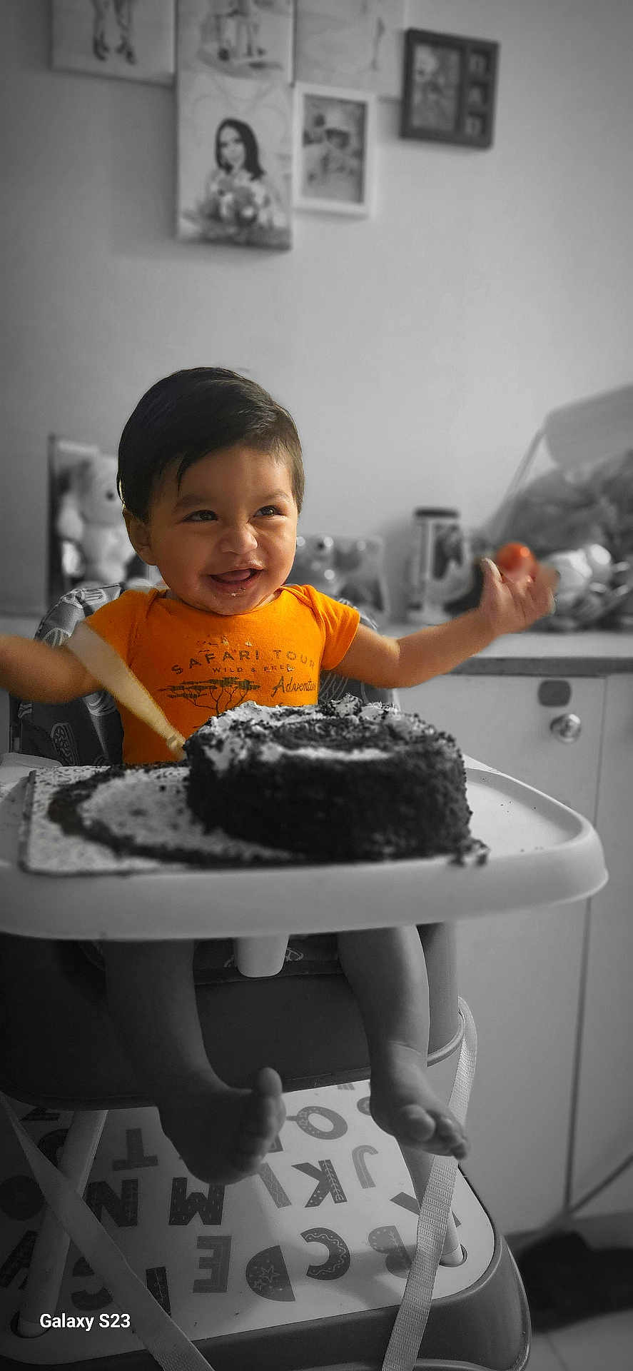 Anthony joined the competition — help win amazing prizes! toddler, child, high_chair, cake, smiling, happy, orange_shirt, food, celebration, birthday, indoors, table, face, arms_raised, feet, photography, monochrome_background, baby, sitting, fun