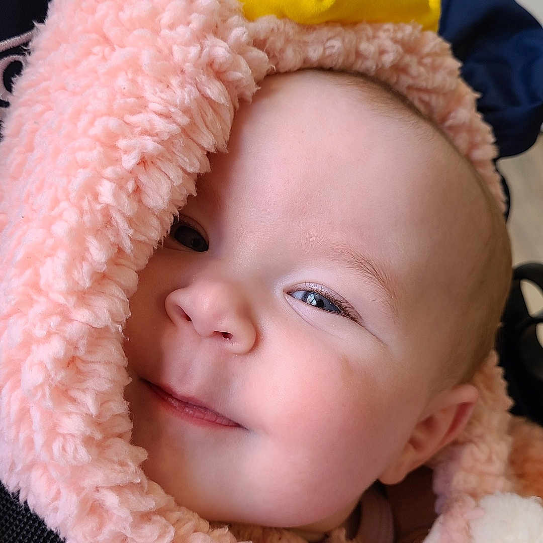 Nina participe au concours pour gagner de l'argent avec cette photo : adorable, baby, cheeks, close_up, clothing, cozy, eyes, hood, infant, lips, navy_background, nose, pink_fur, pom_poms, portrait, safety_strap, smile, soft_texture, stroller, yellow_hat