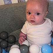 Charlie is registered to the contest to win money with this photo: baby, child, infant, ball_pit, plastic_balls, crib, white_clothing, blue_balls, gray_balls, indoor, person, cute, seated, looking, curious, face, head, small_hand, soft_lighting, closeup