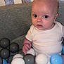 baby, child, infant, ball_pit, plastic_balls, crib, white_clothing, blue_balls, gray_balls, indoor, person, cute, seated, looking, curious, face, head, small_hand, soft_lighting, closeup